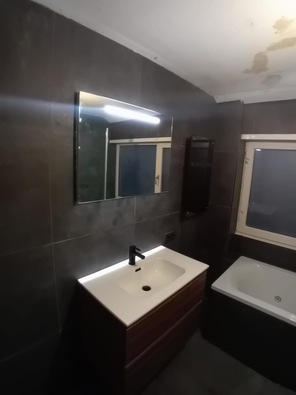Afgewerkte badkamer met donkere tegels, verlichte spiegel en wastafelmeubel