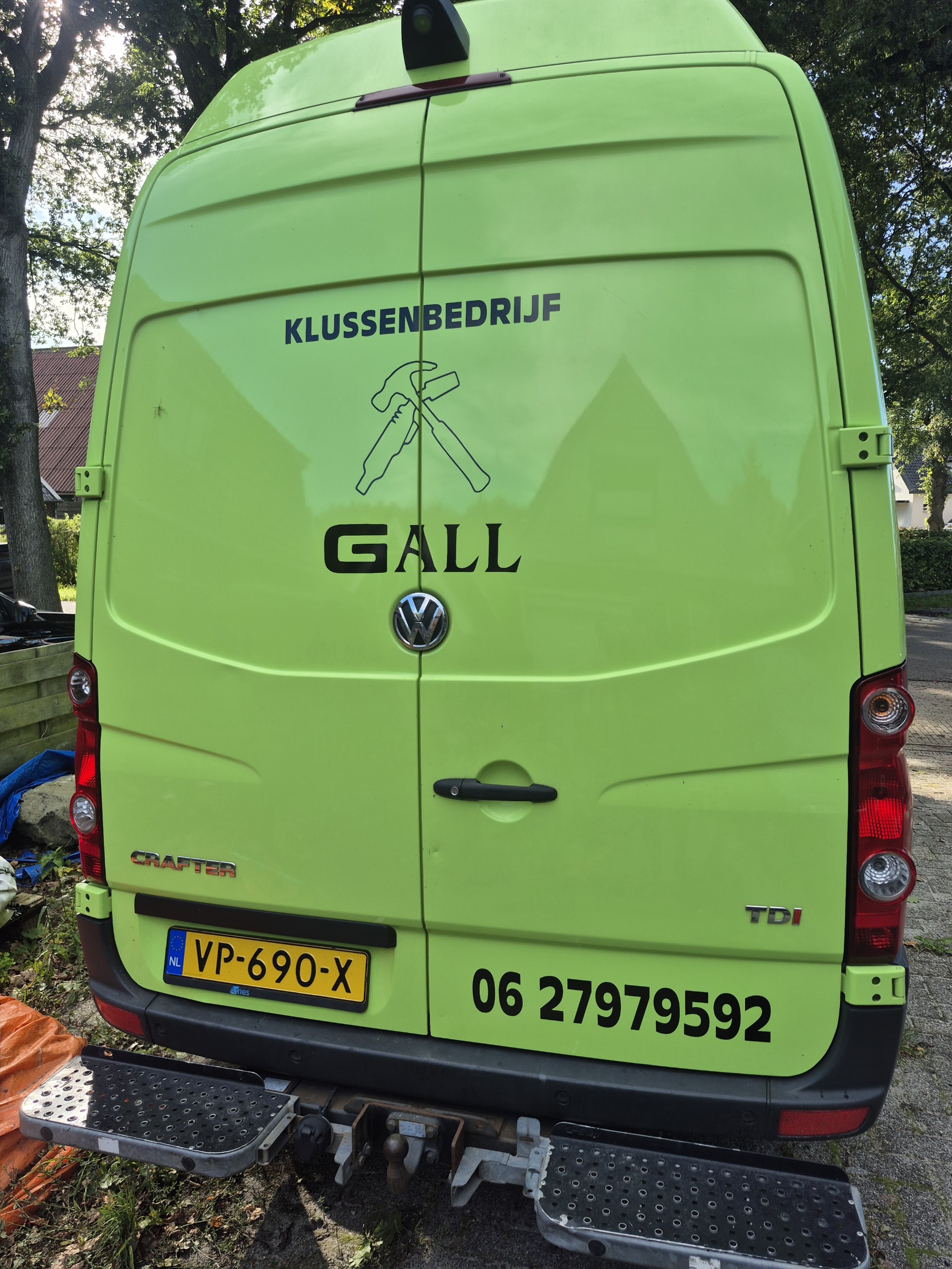 Achterkant van de limoengroene werkbus met het logo van Klussenbedrijf Gall en het telefoonnummer